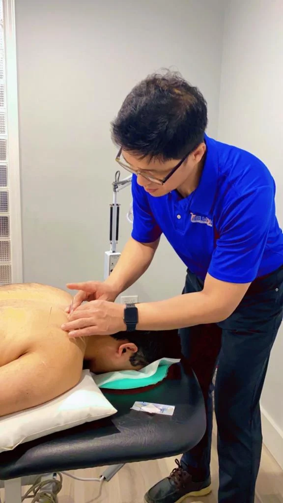 A practitioner performing traditional Chinese medicine acupuncture therapy on a patient's lower back.