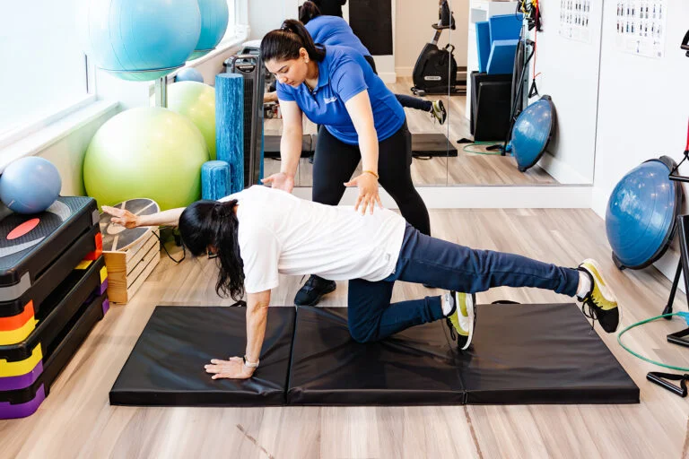 A female physical therapist guiding a patient through pelvic floor and core rehabilitation exercises on a mat.