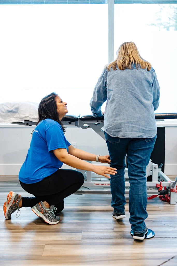 A female physiotherapist assessing a patient's knee and leg movement for osteoarthritis treatment at Belmont Clinic.